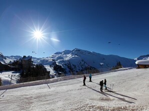 Une piste de ski enneigée avec des skieurs, un ciel dégagé et des montagnes en arrière-plan.