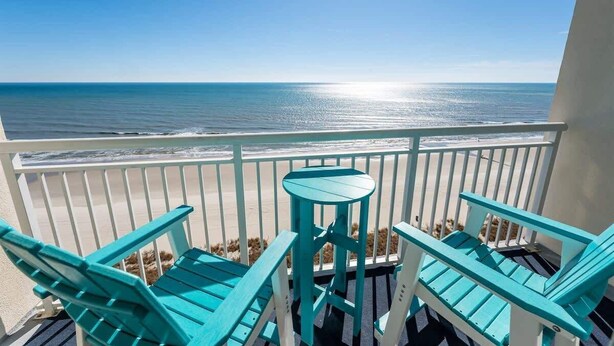 A balcony with turquoise chairs and a small table, overlooking a beach with a clear view of the ocean. - Amazing Beachfront 1Bedroom at Bay Watch with Pool (North Myrtle Beach)