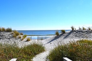 A sandy beach path leading to the ocean, with a fence and vegetation in the foreground.