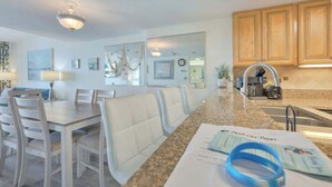 Eine moderne Küche mit Granit-Arbeitsplatten, Holzschränken und einem Essbereich mit weißen Stühlen und einem Tisch.