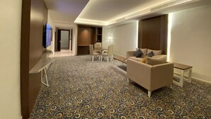 A hotel room with a modern design, featuring a sofa, a dining table, and a TV mounted on the wall. - Al Diyafa Serviced Apartments  الضيافة للشقق المخدومة (Al-Hofuf)