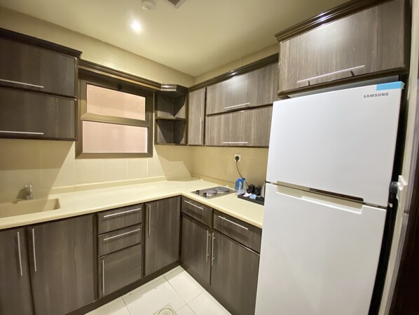 A modern kitchen with dark wood cabinets, a white refrigerator, and a beige countertop.