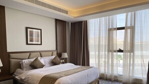 A hotel room with a large bed, a nightstand, a lamp, and a window with sheer curtains. - Al Diyafa Serviced Apartments  الضيافة للشقق المخدومة (Al-Hofuf)