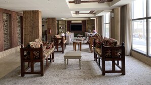 A spacious lobby with wooden furniture, a central seating area, and large windows offering a view of the street. - Al Diyafa Serviced Apartments  الضيافة للشقق المخدومة (Al-Hofuf)