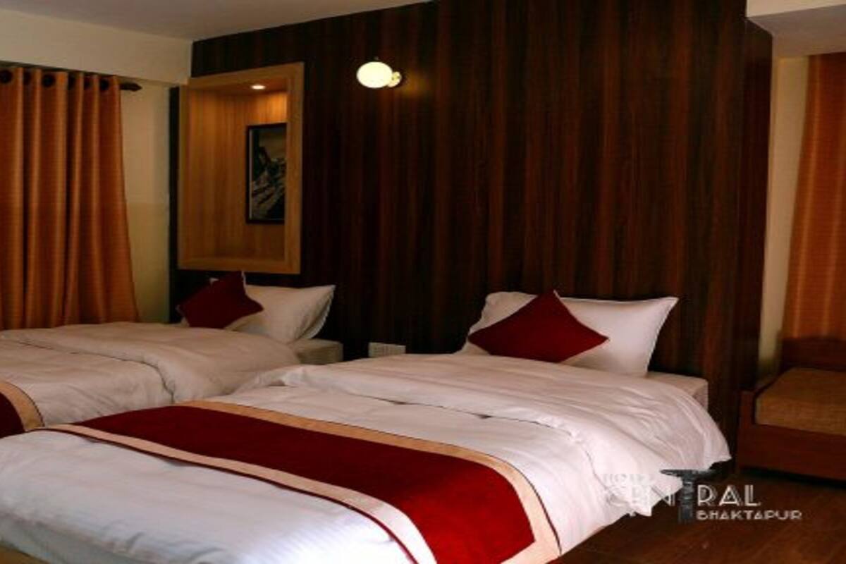 Quarto de hotel com duas camas, painéis de cabeceira em madeira, um quadro na parede e um toque de vermelho nas camas.
