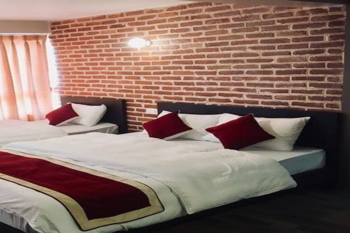 Quarto de hotel com duas camas, parede de tijolos e janela com cortinas.