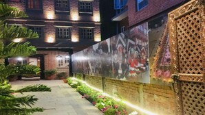 A courtyard with a brick building, a decorative gate, and a wall with a mural. - MeroStay 220 Hotel CBR (Bhaktapur)