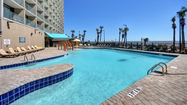 Ein Hotelpoolbereich mit klarem, blauem Wasser, Liegestühlen und einem von Palmen gesäumten Weg.