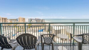 Ein Balkon mit Stühlen und Tisch, der Blick auf Strand und Stadt bietet.