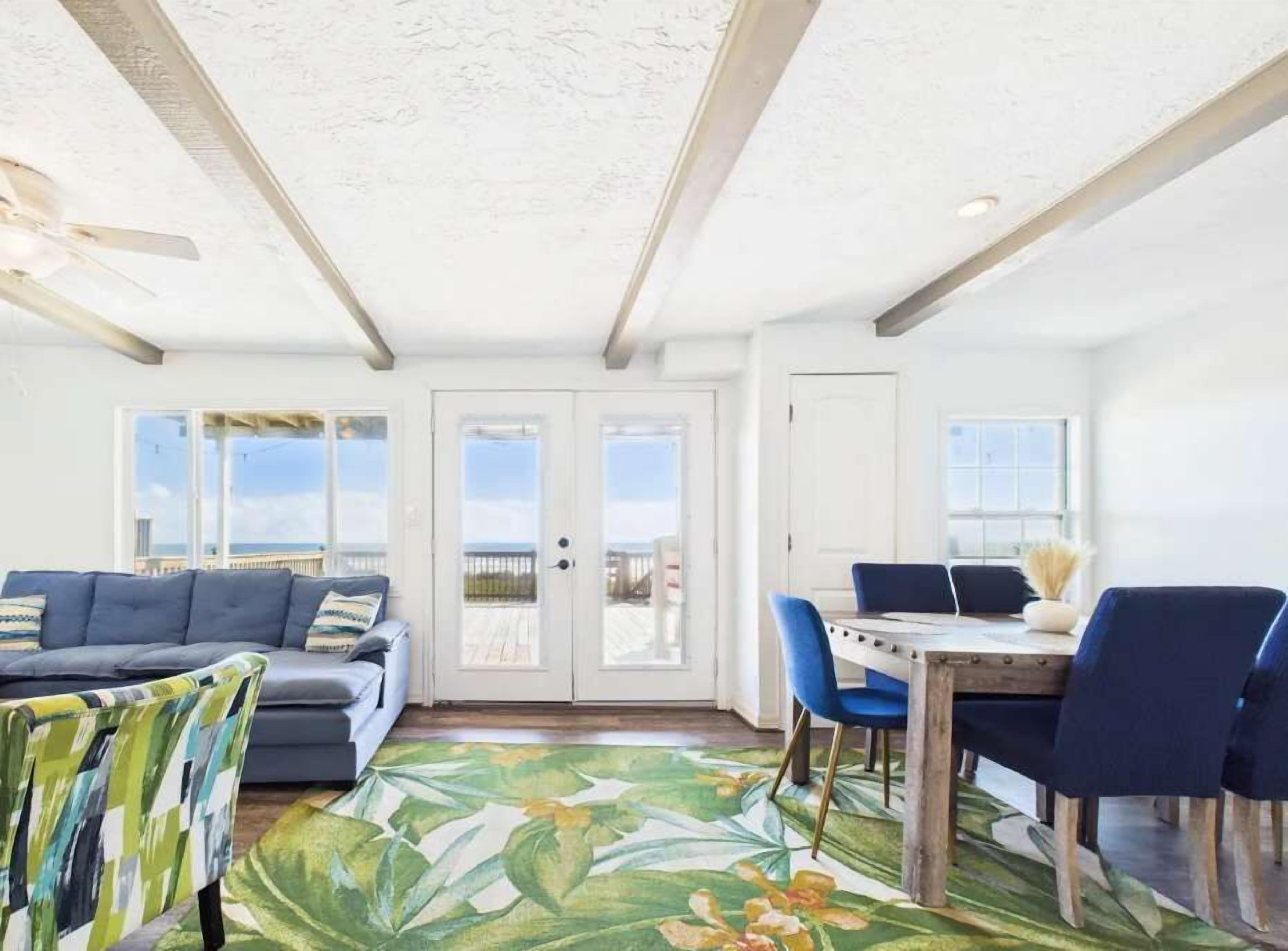 A room with a ceiling fan, a sofa, a dining table with chairs, and a view through a glass door.