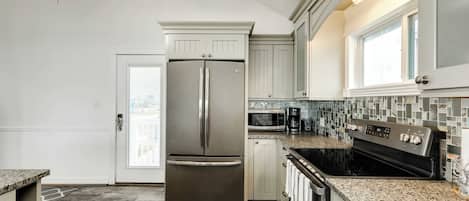 A kitchen with a stainless steel refrigerator, a microwave, a stove, and a tiled backsplash.