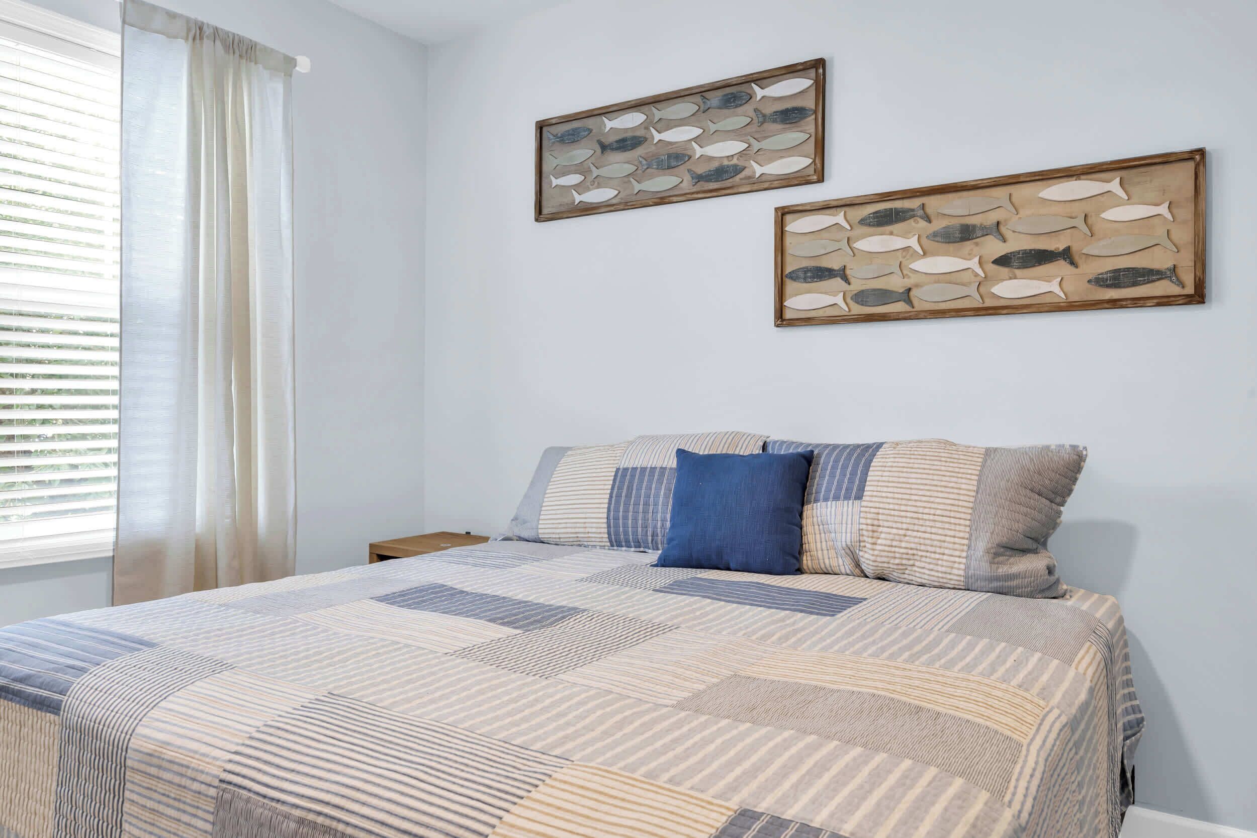 A bedroom with a bed, two pillows, a nightstand, and two framed fish wall art pieces.