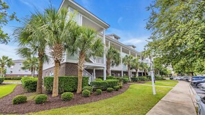 A multi-story residential building with a covered porch, palm trees, and a well-maintained lawn. - Newly Updated Condo for Beach Pool and Golf Lovers (North Myrtle Beach)