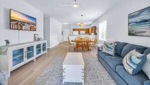 A modern living room with a sofa, coffee table, and dining area with wooden chairs. - Newly Updated Condo for Beach Pool and Golf Lovers (North Myrtle Beach)