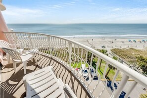 Un balcon avec des chaises blanches et une vue sur la plage et l’océan.
