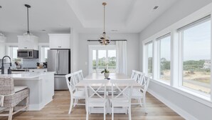 Una cocina moderna con armarios blancos, una isla central y un comedor con sillas y una mesa blancos.