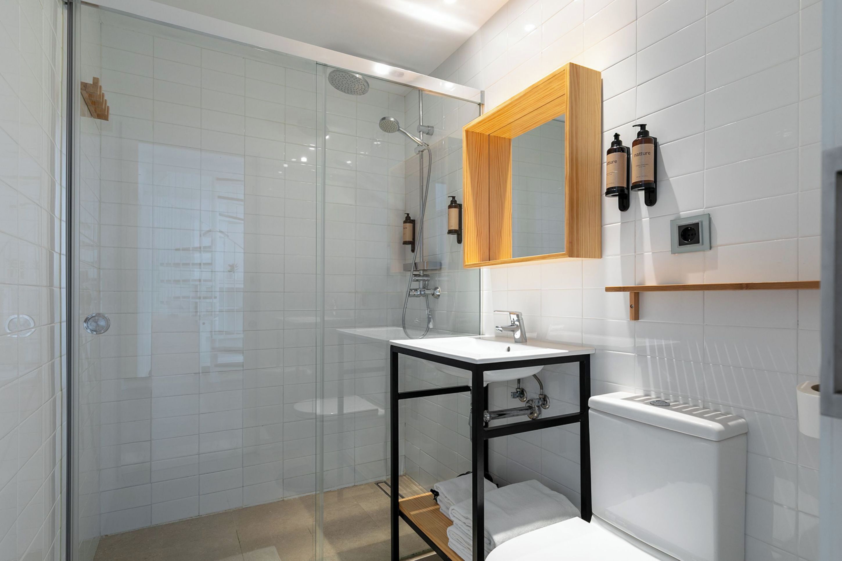 A modern bathroom with a glass shower enclosure, a white sink with a black frame, and a wooden medicine cabinet above the sink.