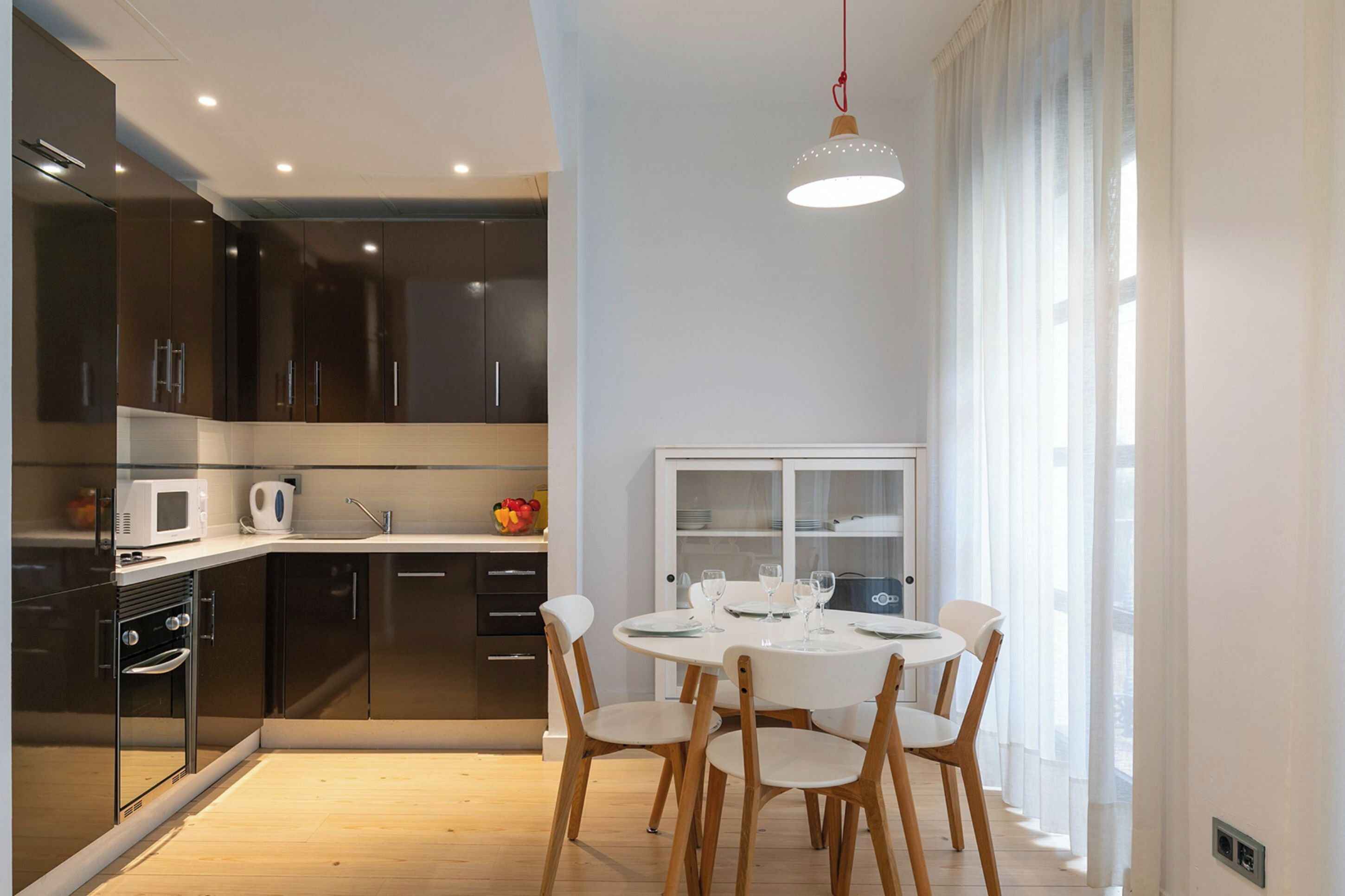 Une cuisine moderne avec des meubles de couleur sombre, un plan de travail blanc et un coin repas comprenant une table ronde et des chaises.