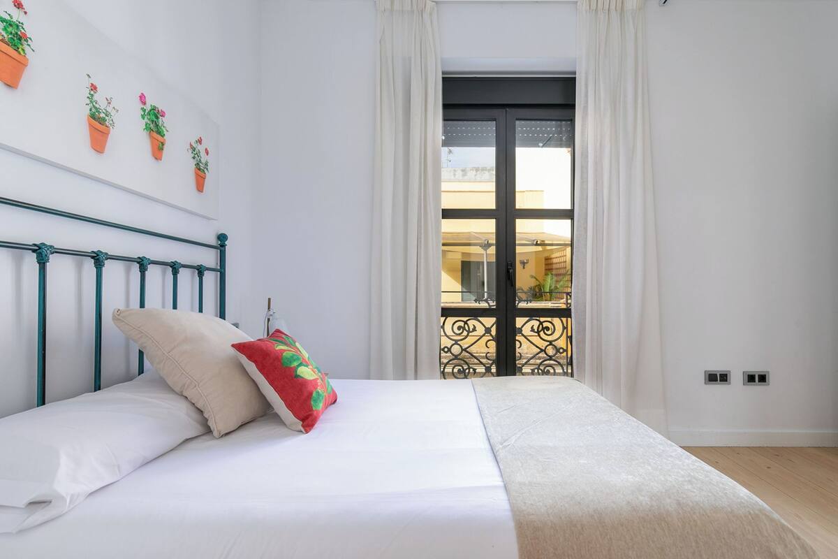 A bedroom with a bed, a headboard, a window with curtains, and a balcony with a railing.