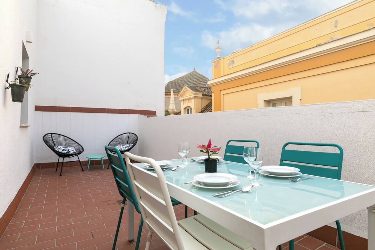 A small outdoor patio with a table set for two, two chairs, and a potted plant.