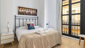 A bedroom with a bed, a nightstand, a lamp, a window with a view of a balcony, and a painting on the wall. - Holiday Rentals Tempa Museo (Seville)