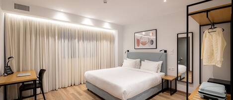 Une chambre d’hôtel moderne équipée d’un grand lit, d’un bureau, d’une chaise, d’une armoire et d’un miroir.