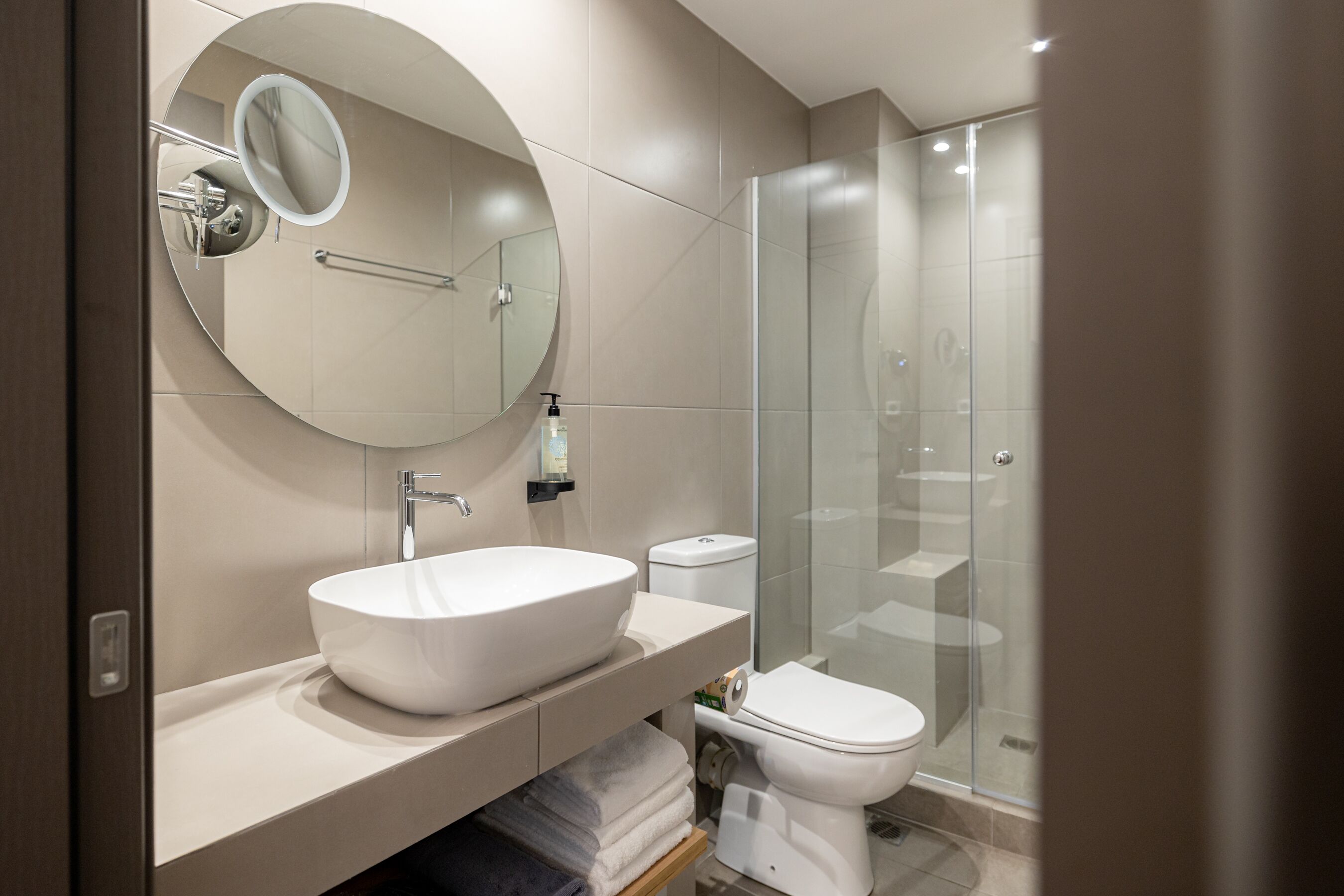 Une salle de bain moderne avec un grand lavabo ovale, un miroir rond, des toilettes et une douche à parois de verre.