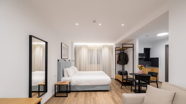Ein modernes Hotelzimmer mit Bett, Schreibtisch, Sofa, Spiegel und einer Küchenzeile.