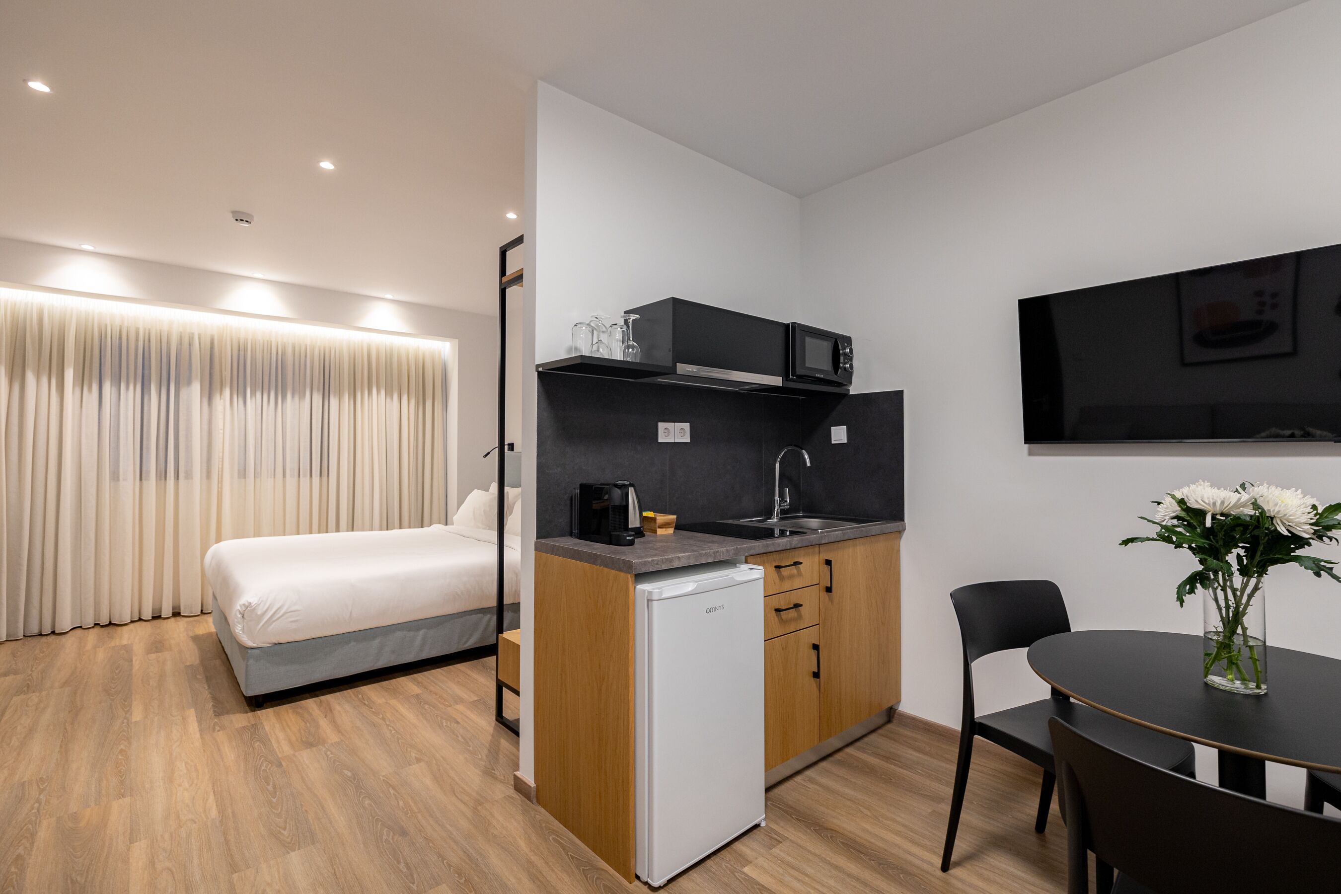 A compact hotel room with a bed, kitchenette, and a dining area.