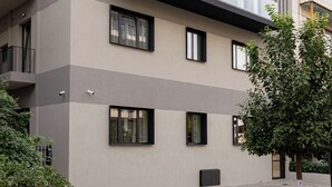 Ein modernes, mehrgeschossiges Gebäude mit Balkonen, einer flachen Dachterrasse und einem gepflasterten Innenhof.
