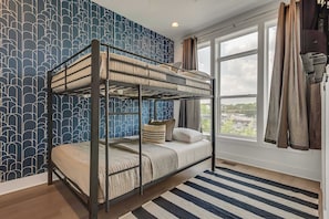 Une chambre avec un lit superposé, un mur décoré d’un motif, une grande fenêtre et un tapis à rayures.