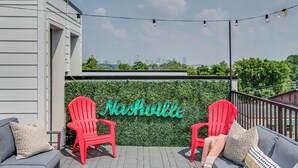 Eine Dachterrasse mit Blick auf die Skyline der Stadt, rote Adirondack-Stühle, eine grüne Wand mit der Aufschrift 'Nashville' und Lichterketten.