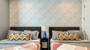 Ein Hotelzimmer mit zwei Betten, einem Nachttisch mit Lampe, gemustertem Wandpapier und einer Tür.