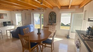 Un salón amplio con techo de madera, una mesa de comedor con sillas, un sofá y una zona de cocina con estufa y armarios.