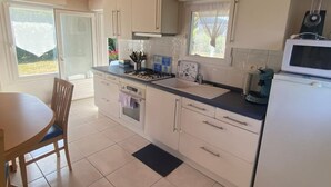 Una cocina moderna con armarios blancos, una estufa, un fregadero y un microondas. Hay una mesa de comedor con sillas y una ventana con vistas al exterior.