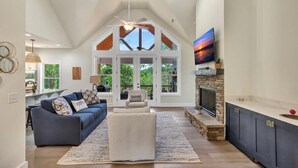 A spacious living room with a high ceiling, a fireplace, and a large TV. - Peninsula Rd - Fun and Relaxation (West Union)