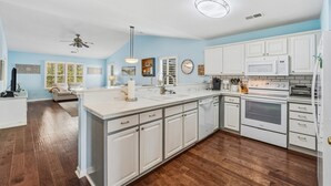 Une cuisine moderne avec des meubles blancs, un îlot central et un four encastré.