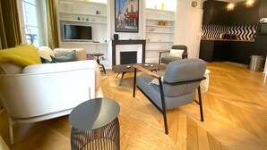 A modern living room with a sofa, armchairs, a TV, and a fireplace. - L'appartement Letac (Paris)