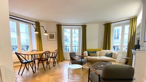 A modern living room with a wooden herringbone floor, a dining area with a wooden table and chairs, a sofa, and a coffee table. - L'appartement Letac (Paris)