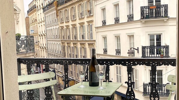 A balcony with a bottle of wine and a glass, overlooking a street with buildings. - L'appartement Letac (Paris)