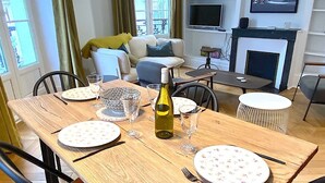 A dining area with a wooden table set for four, surrounded by chairs. There is a bottle of wine on the table. - L'appartement Letac (Paris)