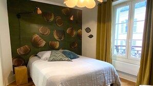 A bedroom with a bed, a nightstand, a window with curtains, and a wall with decorative shells. - L'appartement Letac (Paris)