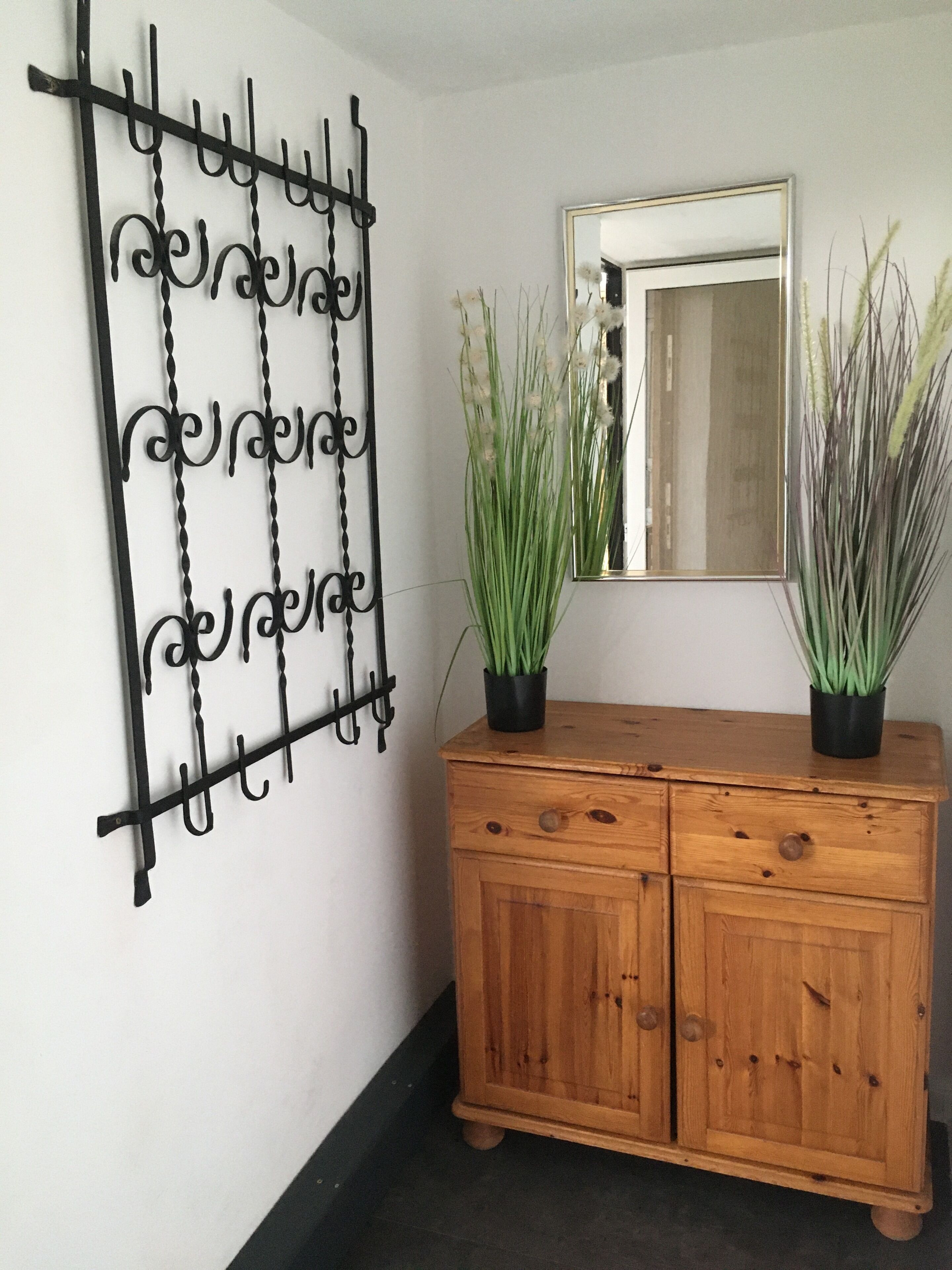A wooden cabinet with two potted plants, a metal wall art piece, and a mirror on the wall.