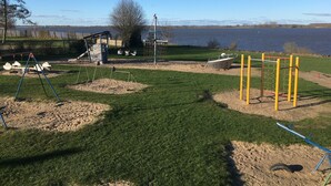 Une aire de jeux avec des balançoires, des toboggans et des structures d’escalade, située près d’un lac.
