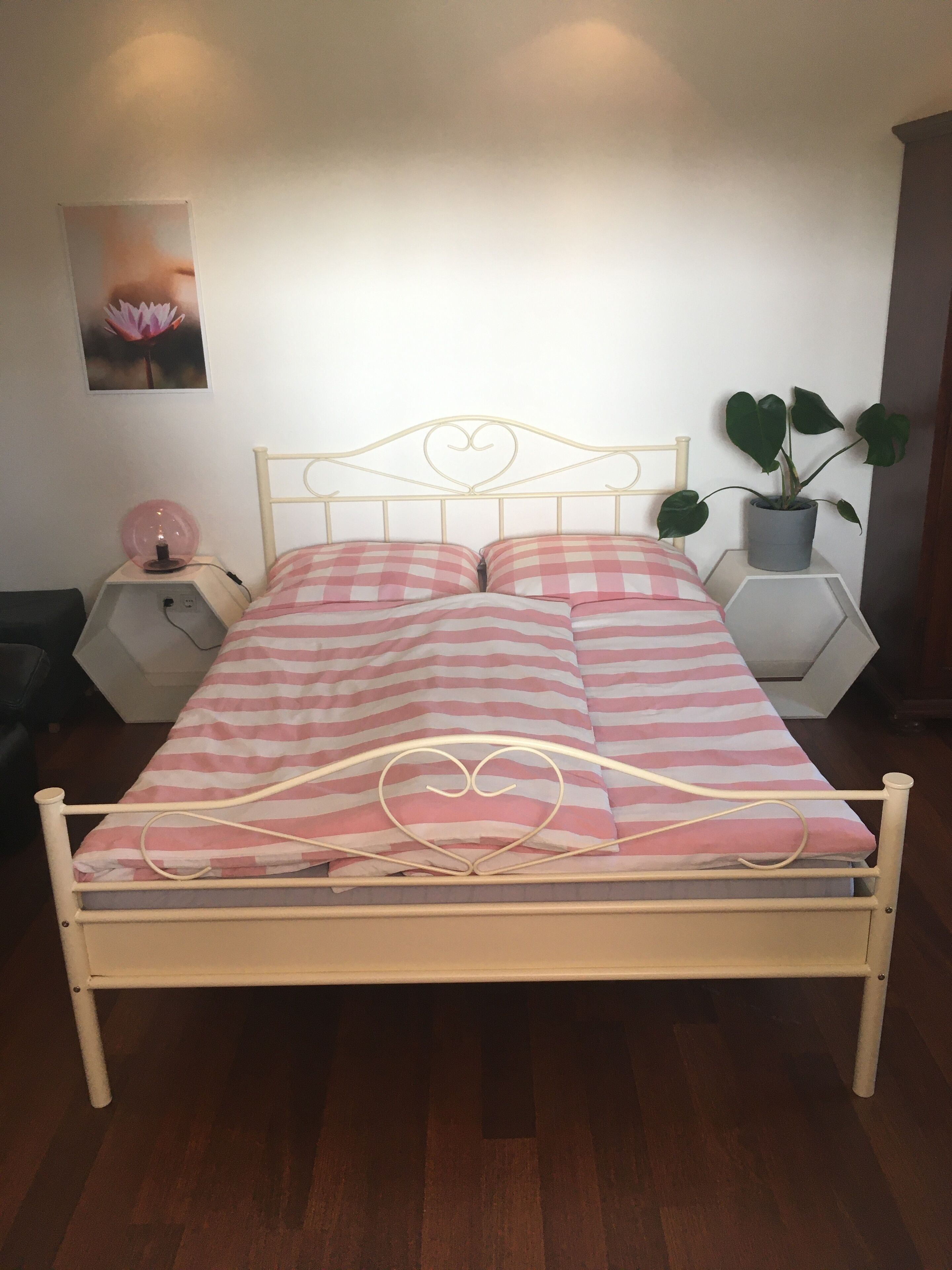 Un lit avec une tête de lit en forme de cœur, une table de chevet avec une lampe et une plante en pot.