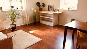 Une pièce lumineuse avec un plancher en bois, un canapé blanc, une table à manger et diverses plantes en pot.