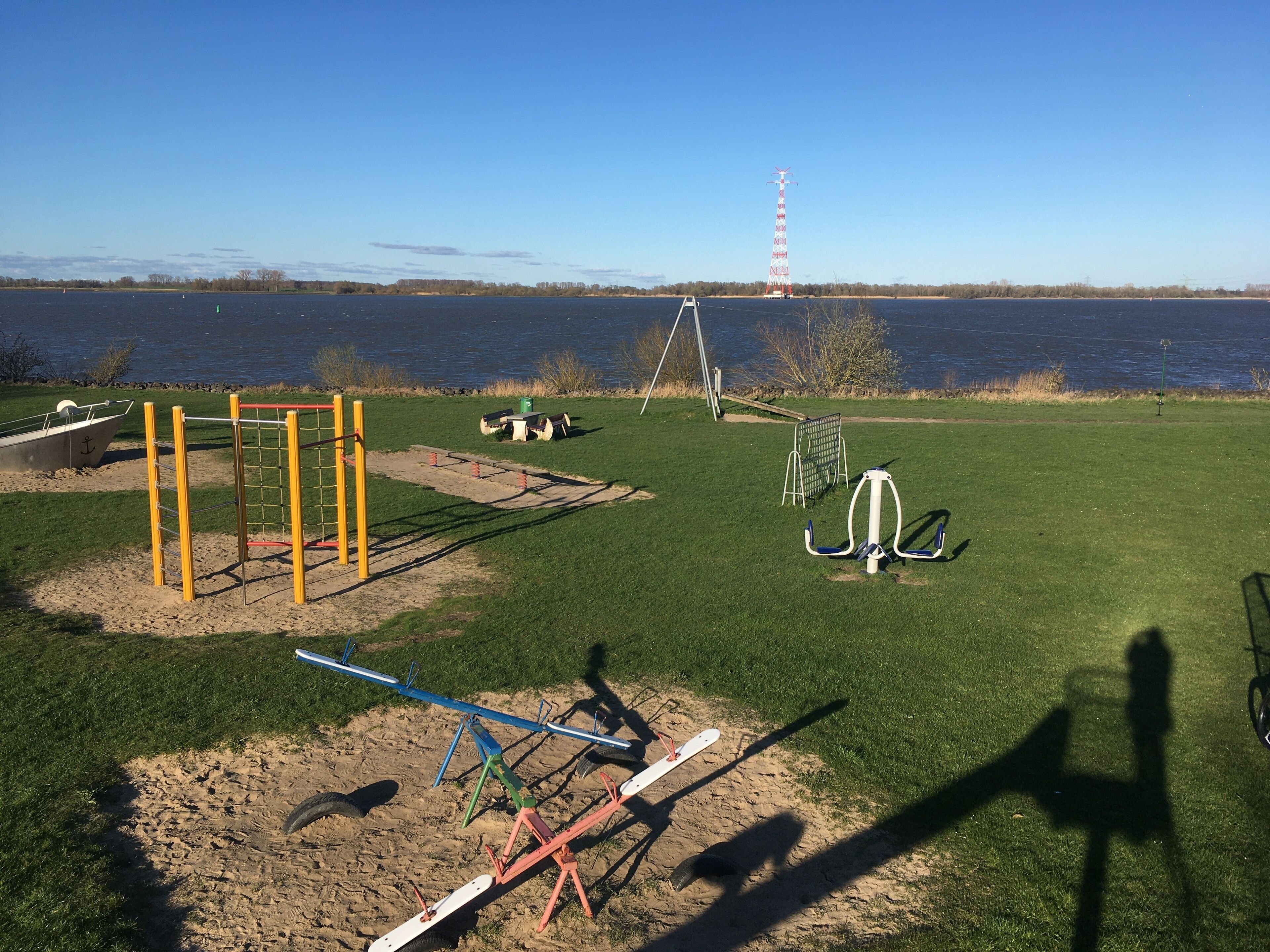 A playground with swings, a seesaw, and a climbing structure near a lake.