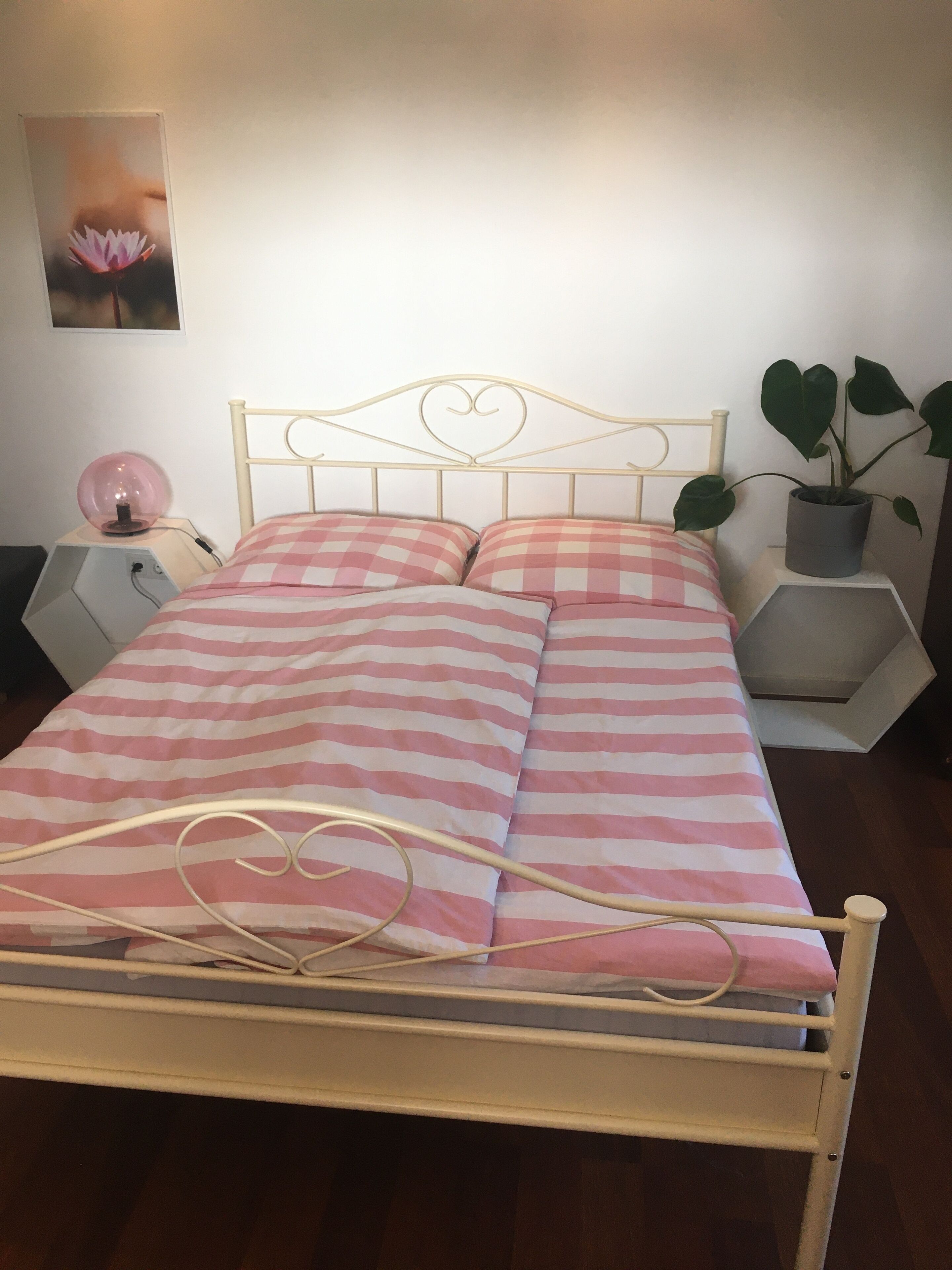 En seng med et ternet pink og hvidt sengetæppe, et hjerteformet sengegavl og et natbord med en lampe.