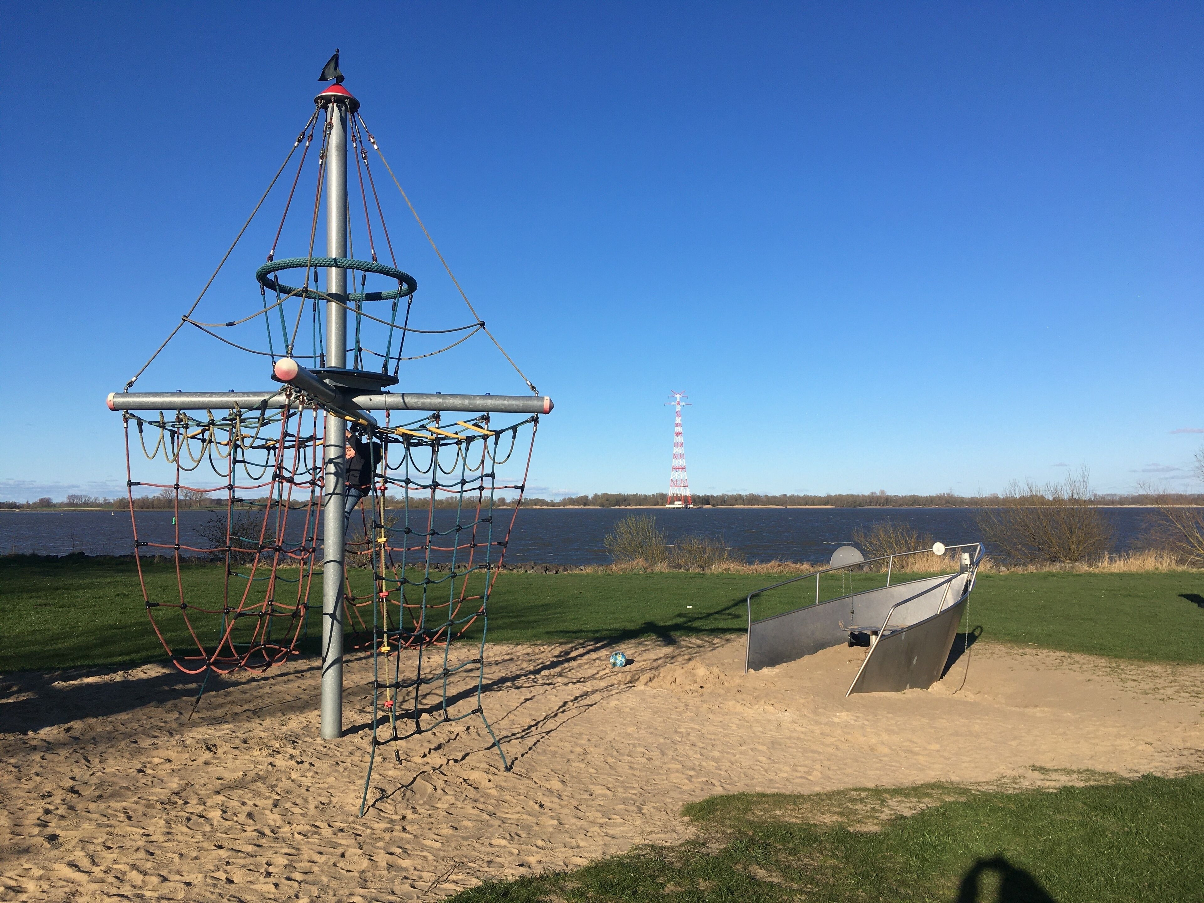 Ein Spielplatz mit einer Kletteranlage und einem Boot im Hintergrund.