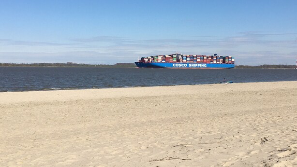 Une plage avec un grand navire bleu amarré dans l'eau, portant l'inscription « COSCO SHIPPING ».